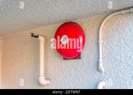 Red fire alarm bell on a painted white textured wall in San Francisco, California Stock Photo