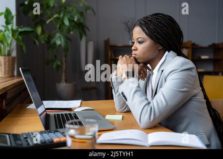 Frustrated african businesswoman looking thoughtfully at open laptop and trying to focus on work Stock Photo