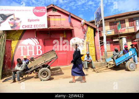 Malagasy men sitting in a trolley waiting for work while a woman is walking by with a heavy bag on her head. Ambohimanga region in central Madagascar. Stock Photo