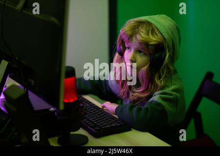 Kid boy hacker, young programmer. Child playing computer games or studying on pc computer. Kid gamer on night neon lighting. Stock Photo