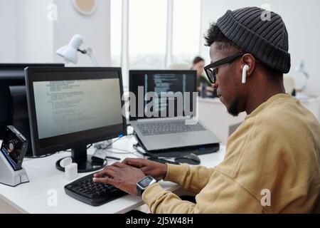 Side view of young male programmer or it developer in casualwear listening to music in earphones while working in office Stock Photo