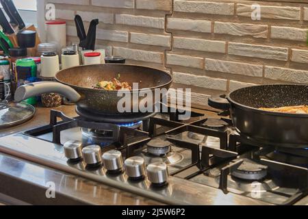Frying pans with fried potatoes, chestnuts, parsley, parmesan on gas stove in the kitchen. Step by step recipe Stock Photo
