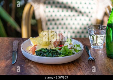 Sourdough toast, poached eggs, salmon, hollandaise, sauteed and fresh vegetables on plate in cafe, close up Stock Photo
