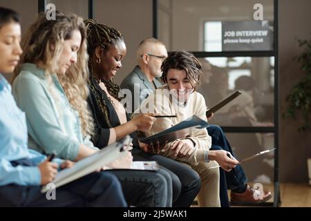 Young man smiling and discussing business contract together with woman while they sitting in waiting room and awaiting interview Stock Photo