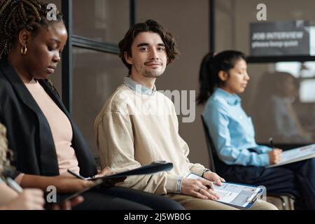 Portrait of young candidate sitting in waiting room with resume and looking at camera Stock Photo