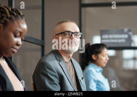 Portrait of mature man in eyeglasses looking at camera while sitting in waiting room of office Stock Photo