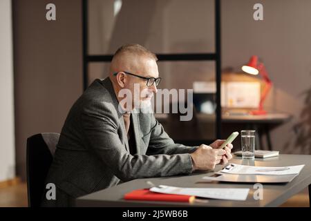 Serious mature candidate for job using mobile phone while sitting at table and waiting for his interview Stock Photo