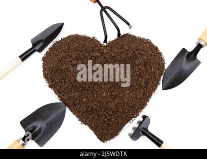Various small garden tools arranged around a heart-shaped pile of soil isolated on white background. Gardening season concept. Stock Photo