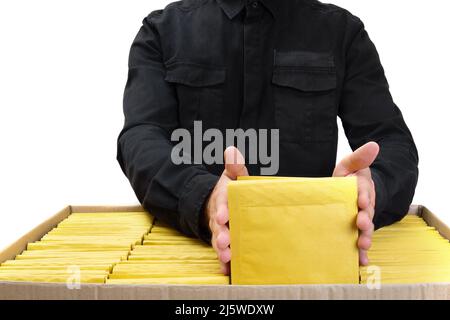 Person in black uniform packing yellow padded envelopes into a large cardboard box isolated on white background. Product inspection and shipping conce Stock Photo