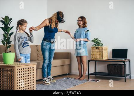 Woman using VR headset glasses virtual reality at home standing on living room with kids Stock Photo