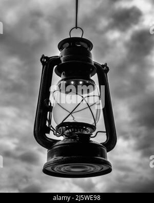A lantern hanging by a thread against a dramatic, black and white sky Stock Photo