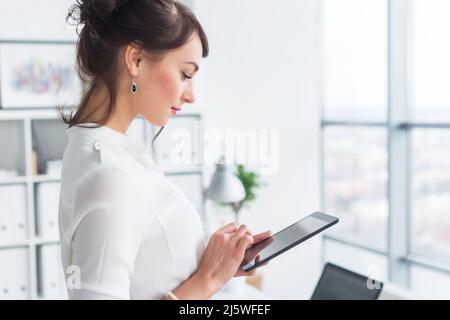 Young smiling female office worker at her workplace reading, browsing news ad messages using tablet computer while having break Stock Photo