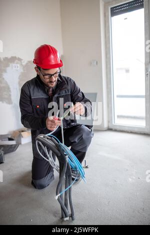 Male electrician in uniform with helmet using pliers to cut electrical wires. Stock Photo