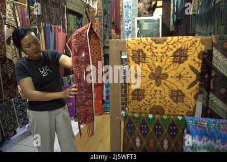 Ni Wayan Sudiati, a traditional clothing artist, giving explanation on a traditional fabric, standing next to traditional clothes called 'kamen gringsing' (sarong) that her village is famously known for, in the traditional village of Tenganan Pegringsingan in Karangasem, Bali, Indonesia. Stock Photo