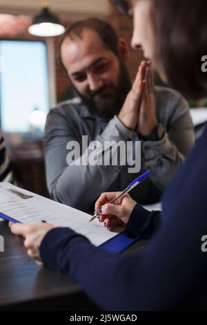 Startup company recruiter reviewing smiling job candidate CV while sitting in office space. Thankful applicant smiling heartily because of career oportunity while woman reading man resume. Stock Photo