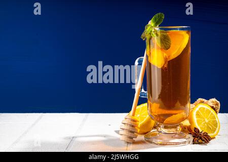 Ginger lemon hot tea drink. One glass cup with traditional autumn winter warm spicy drink with honey, lemon and ginger slices, on dark blue and white Stock Photo