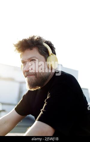 40-year-old Nordic man with beard and headphones looking to the side outdoors with sunset light from behind Stock Photo