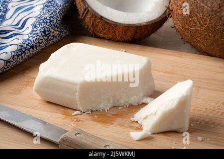 Piece of creamed coconut, coconut butter, on a cutting board close up and fresh coconut on the background Stock Photo