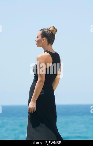 Rear view of young woman wearing black dress standing on the beach Stock Photo