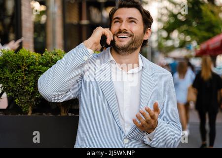 Young man gesturing and talking on mobile phone while standing outdoors Stock Photo