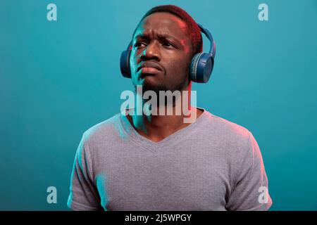 Model listening to mp3 music on headphones and feeling pensive in front of camera. Thoughtful guy enjoying modern record song on audio headset to relax in studio. Stereo sound on earphones Stock Photo