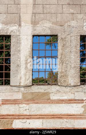 Three trellised windows in block wall with blue sky on other side. Stock Photo