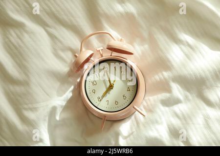 Pink alarm clock on the bed in the morning Stock Photo