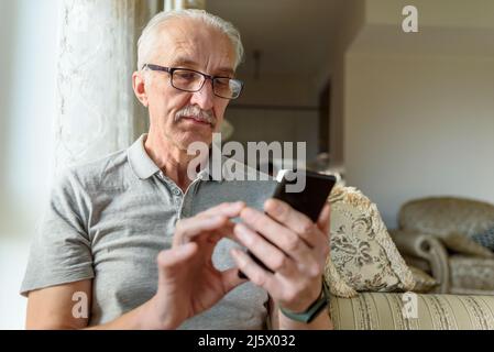Senior man in eyeglasses using mobile phone at home Stock Photo