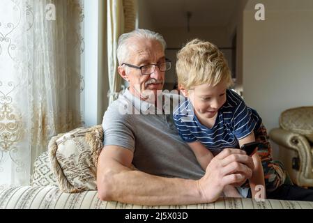 Grandfather with grandson using mobile phone. Looking video, making call Stock Photo