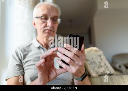 Senior man in eyeglasses using mobile phone at home Stock Photo