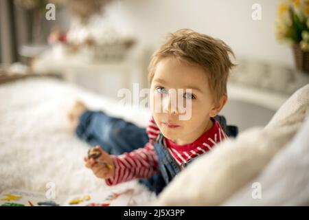 Cute child at home with little newborn chicks, eating chocolate candy in bed, happy kid Stock Photo