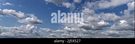 Cumulus clouds illuminated by the rays of the sun float across the blue sky. Stock Photo