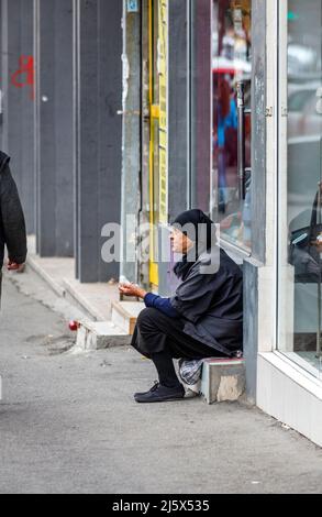 A poor old woman dressed in black and a headscarf sits in a shop doorway begging by the roadside in Bucharest, capital city of Romania, central Europe Stock Photo