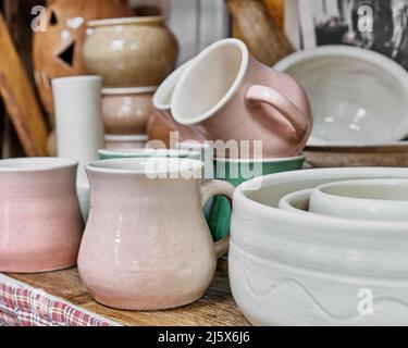 Mugs, plates and other ceramic utensils made of white clay, standing on wood table. Stock Photo