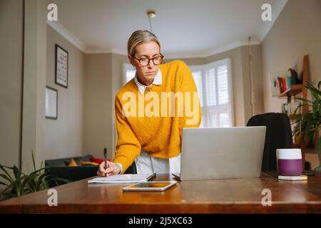 Caucasian female working from home writing on document  Stock Photo