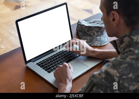 Army. Young soldier working with a laptop computer with blank screen on black background. Stock Photo