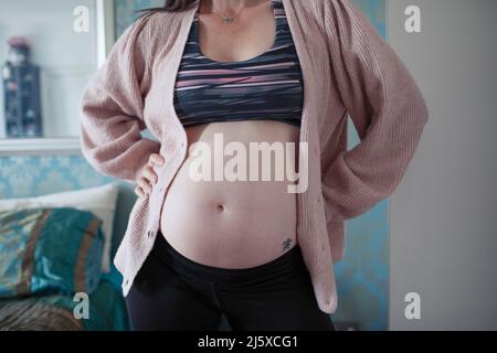 Pregnant woman in sports bra using smart phone in doorway Stock Photo -  Alamy