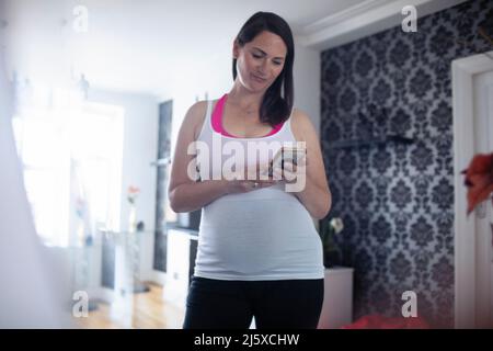 Pregnant woman in tank top using smart phone Stock Photo