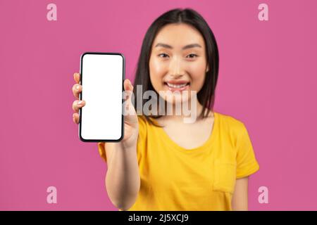 Cool offer. Portrait of happy asian woman holding cellphone with blank screen in hand, showing device to camera, mockup Stock Photo