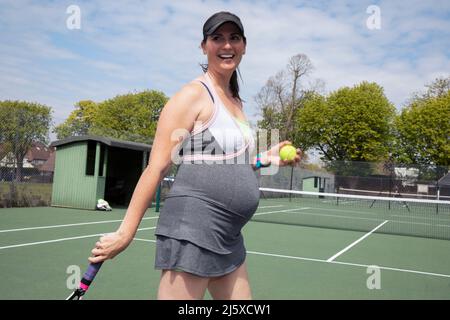 Happy pregnant woman playing tennis on sunny tennis court Stock Photo