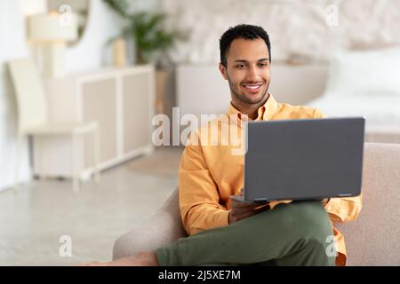 Happy Arab man using laptop sitting on sofa at home Stock Photo