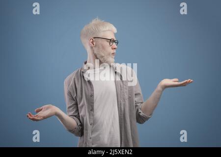 Making choice. Young albino man making scales with his empty hands, doubtful guy comparing options, copy space Stock Photo