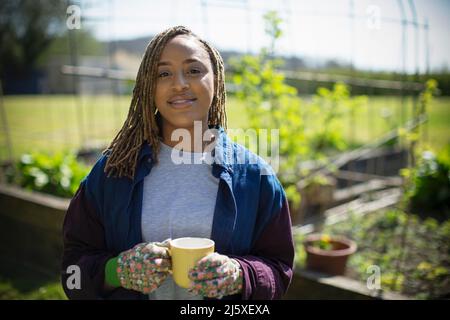 Portrait smiling young woman drinking tea in sunny garden Stock Photo