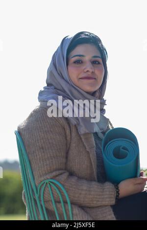 Portrait smiling young Muslim woman in hijab with yoga mat Stock Photo