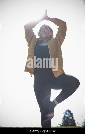 Serene young woman practicing yoga tree pose in sunlight Stock Photo