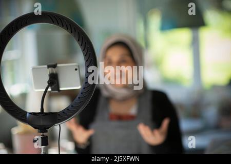 Young female Muslim influencer vlogging with camera phone Stock Photo