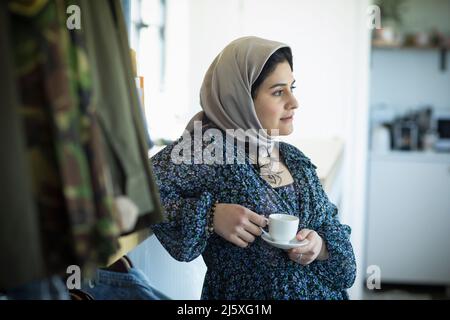 Thoughtful young Muslim woman in hijab drinking coffee Stock Photo