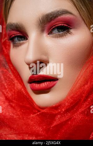 Close up view of young woman with red eye shadow and tulle cloth looking at camera Stock Photo