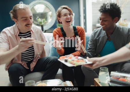 Happy friends sharing sushi in living room Stock Photo