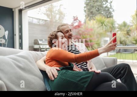 Playful young couple taking selfie with smart phone on sofa Stock Photo